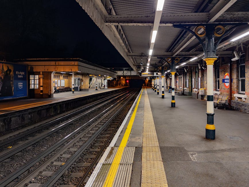 The image depicts a section of Golders Green station platform beneath an elevated structure with a decorative white scalloped edge canopy, providing partial shade. There are three wooden benches with